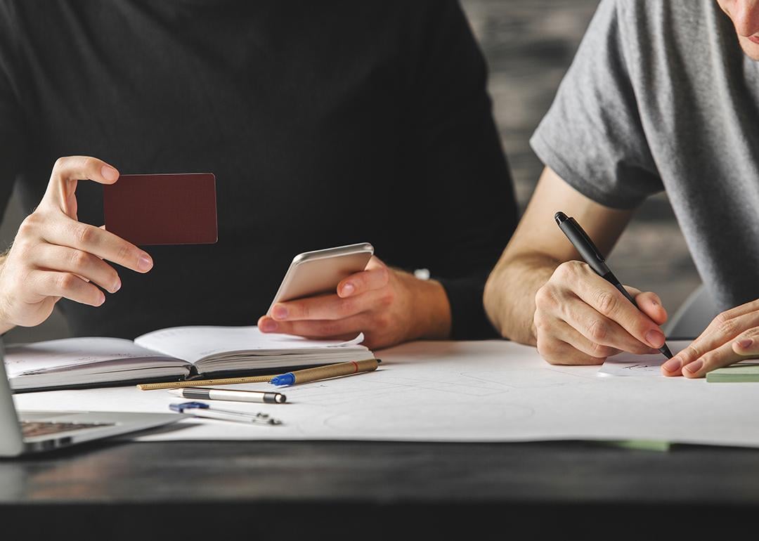 Young man holding credit card beside another person writing down information.