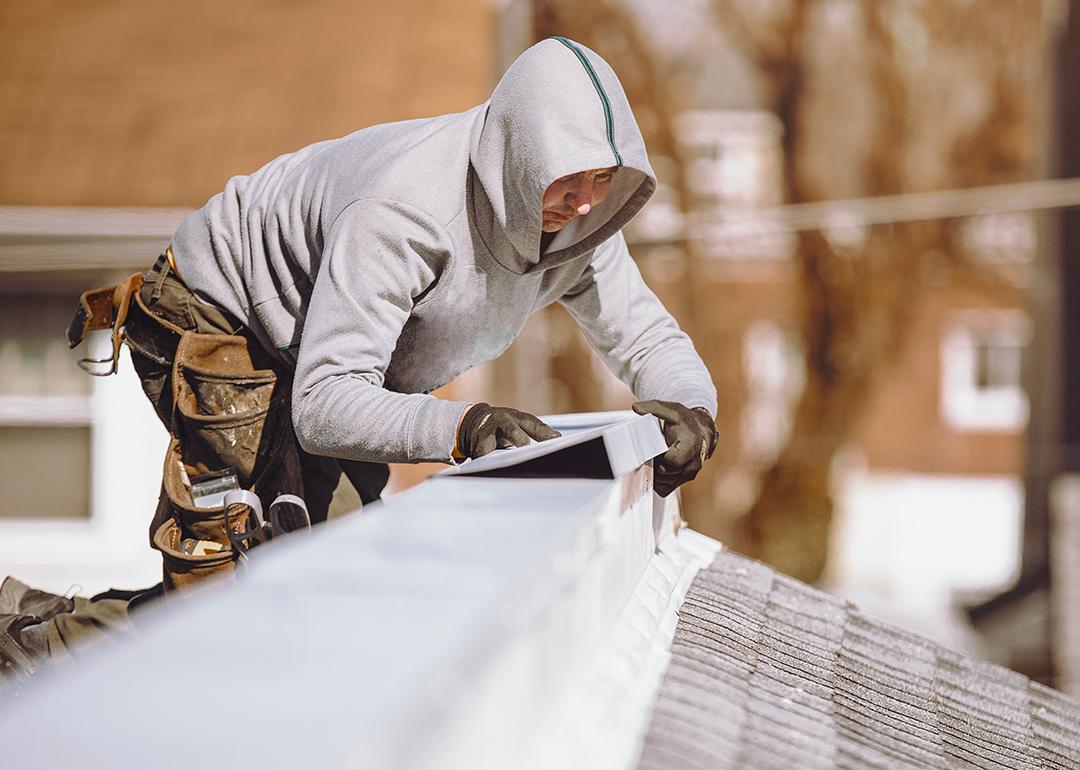 A repairman putting a metal ridge on top of a roof.