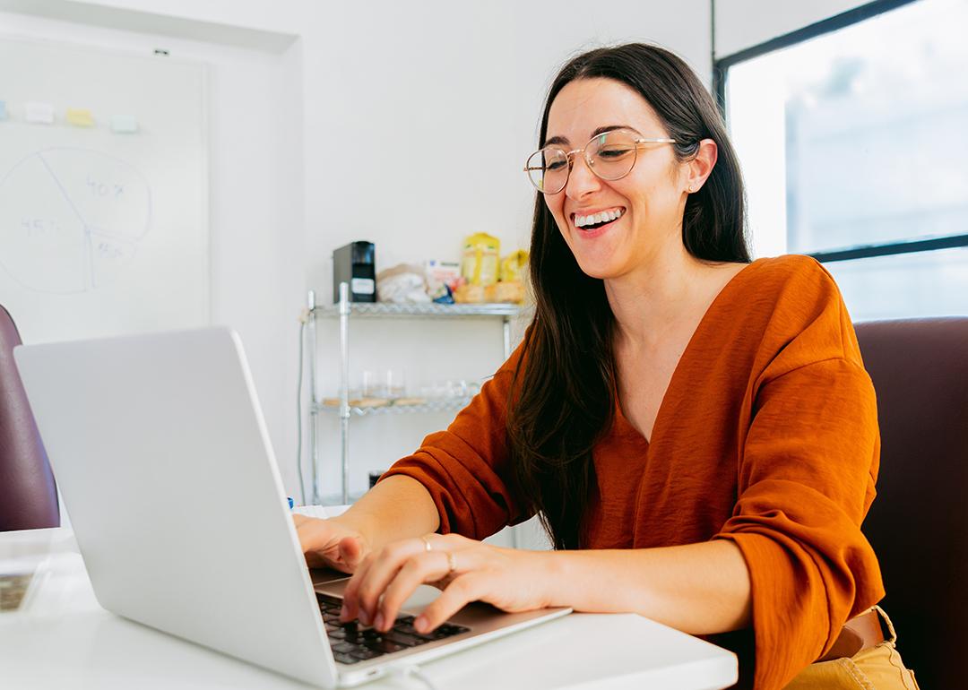 A young Latina woman happily types on a laptop computer.