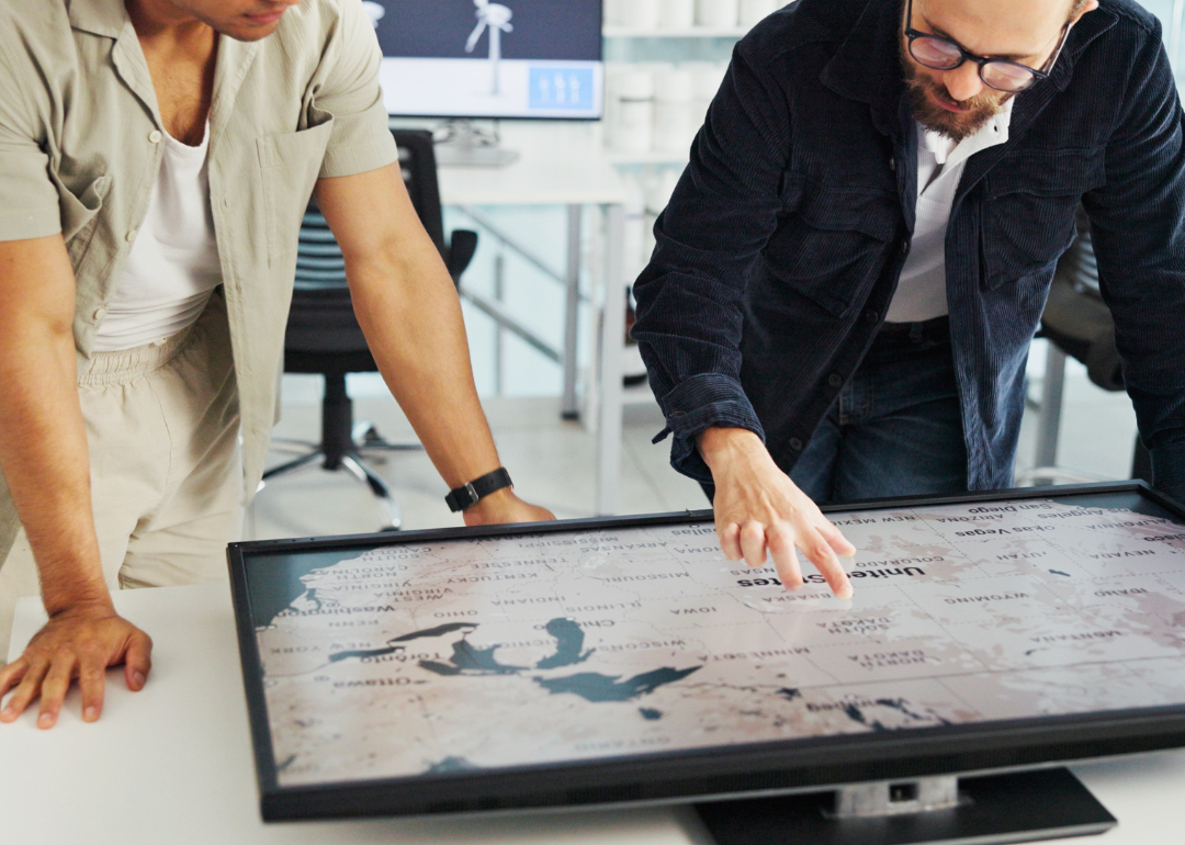 Two people looking at a U.S. map on a screen that is flat on a table in front of them.