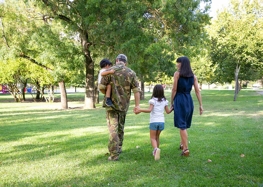 Back view of happy family walking together in a park. The father is wearing camouflage military uniform.