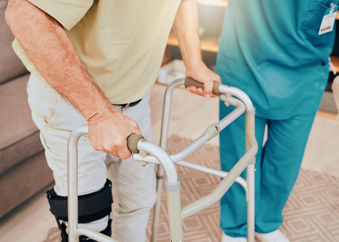 A senior man using a walker during a physiotherapy session assisted by a caregiver.