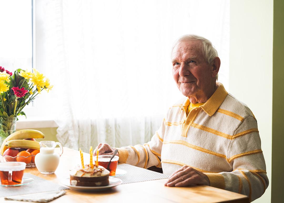 A happy senior old man seated by a dining table with cake.