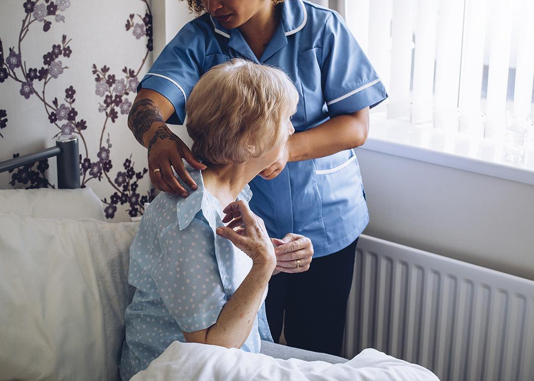 A home caregiver helping a senior woman get dressed in bed.