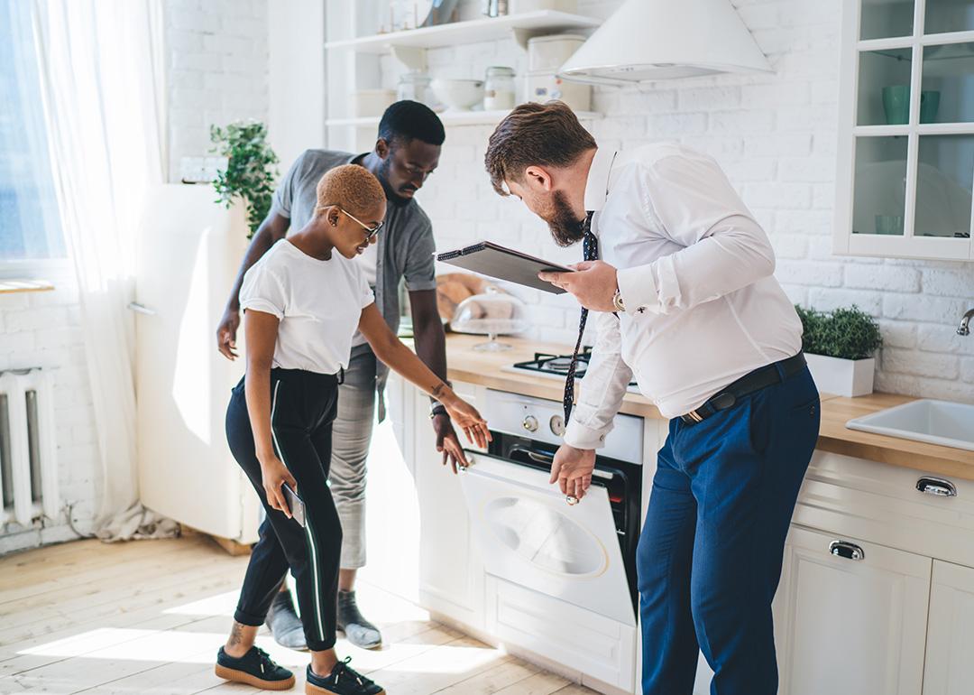 Three people inspecting an oven together in a kitchen area.