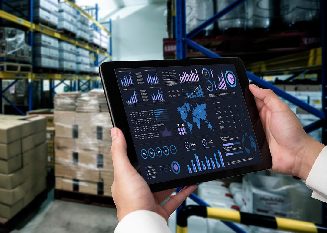 A business data dashboard in an iPad is shown and held by a marketing officer in a stock room.