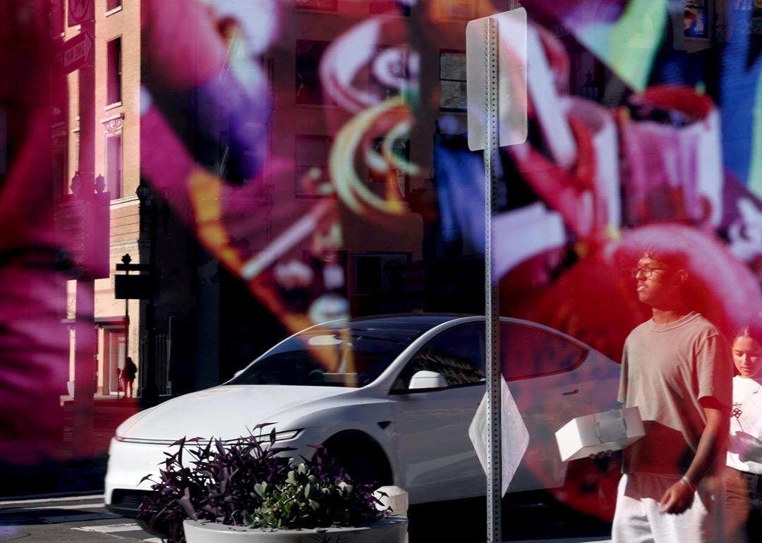 A Tesla car and pedestrians caught in a reflection on a storefront window.