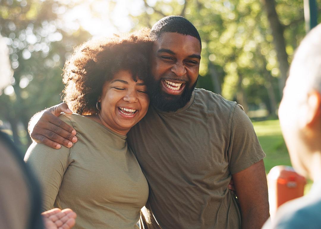 A happy Black couple hug and laugh outdoors.