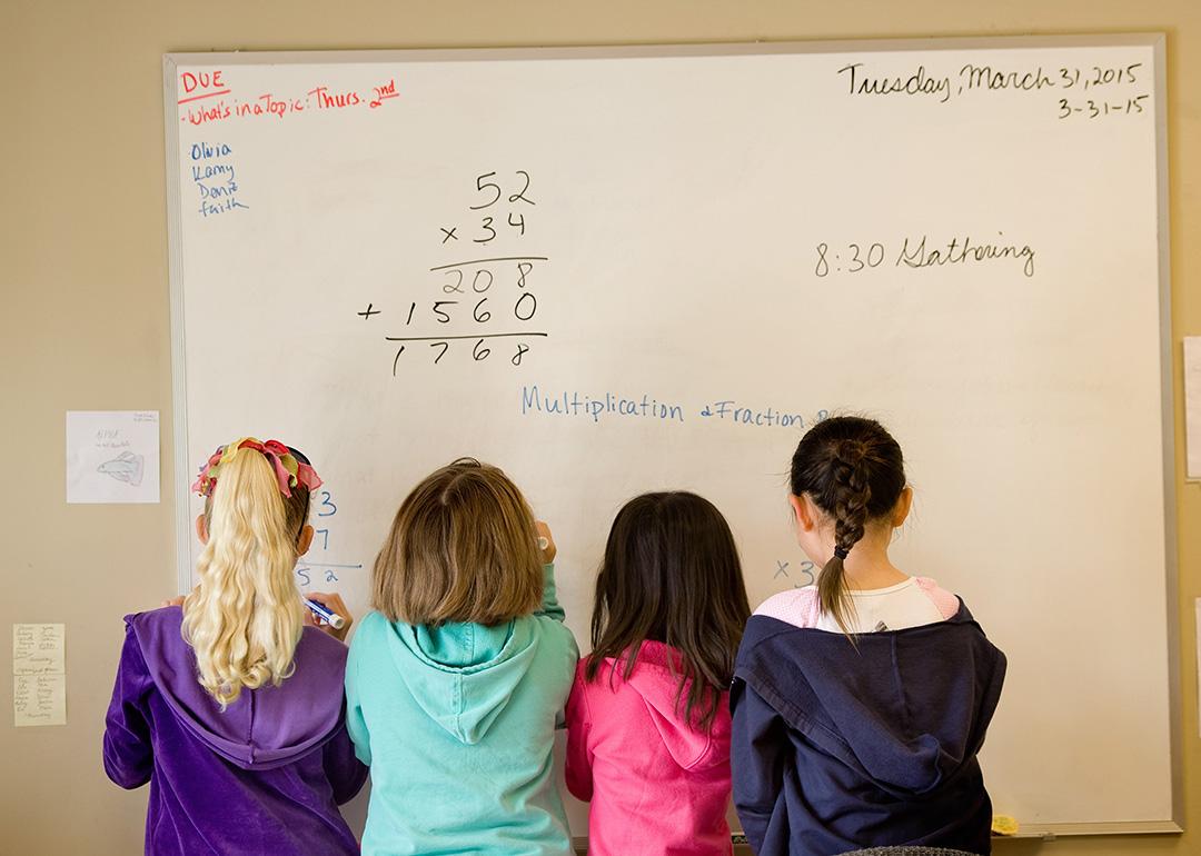 A group of children working to solve math problems on a whiteboard.