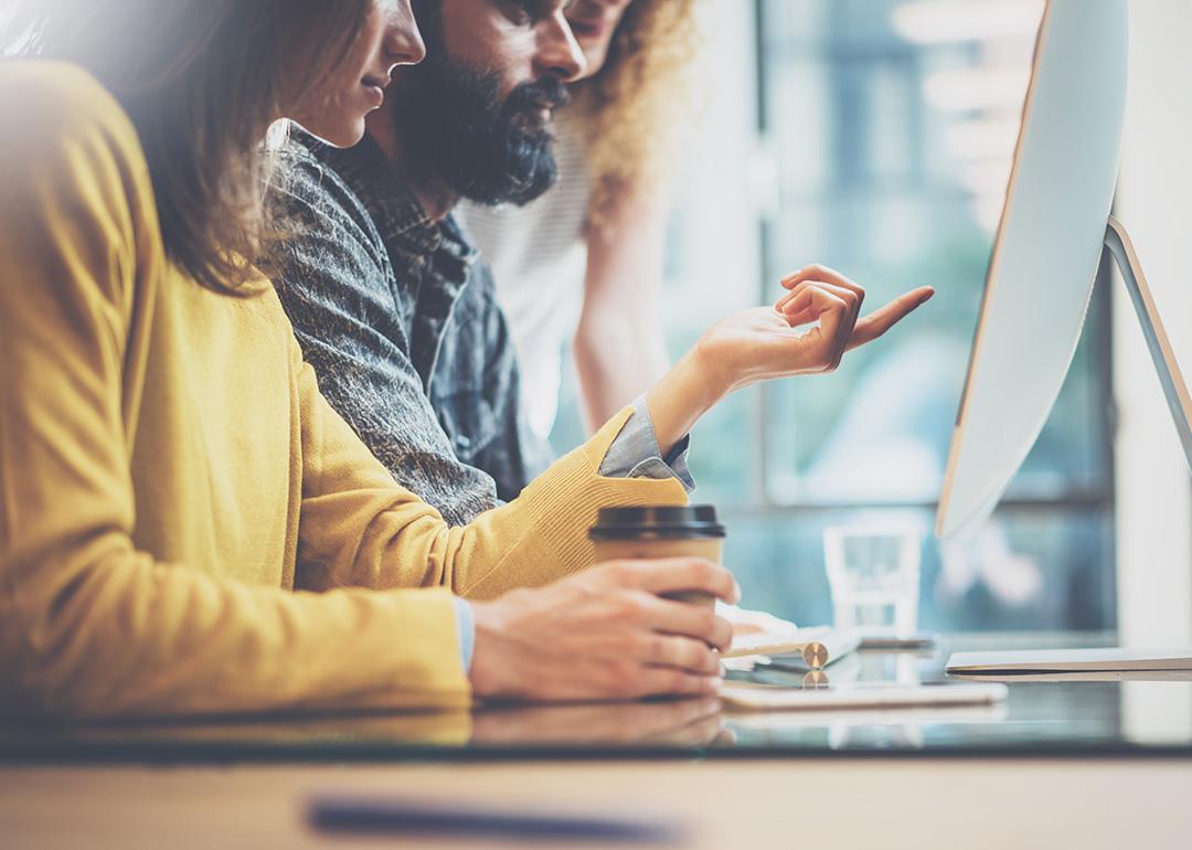 A group of coworkers pointing at a computer monitor while accessing the internet in their office.