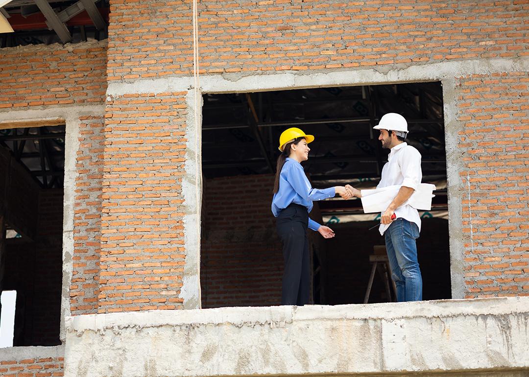 An architect and contractor shaking hands on site for a project.