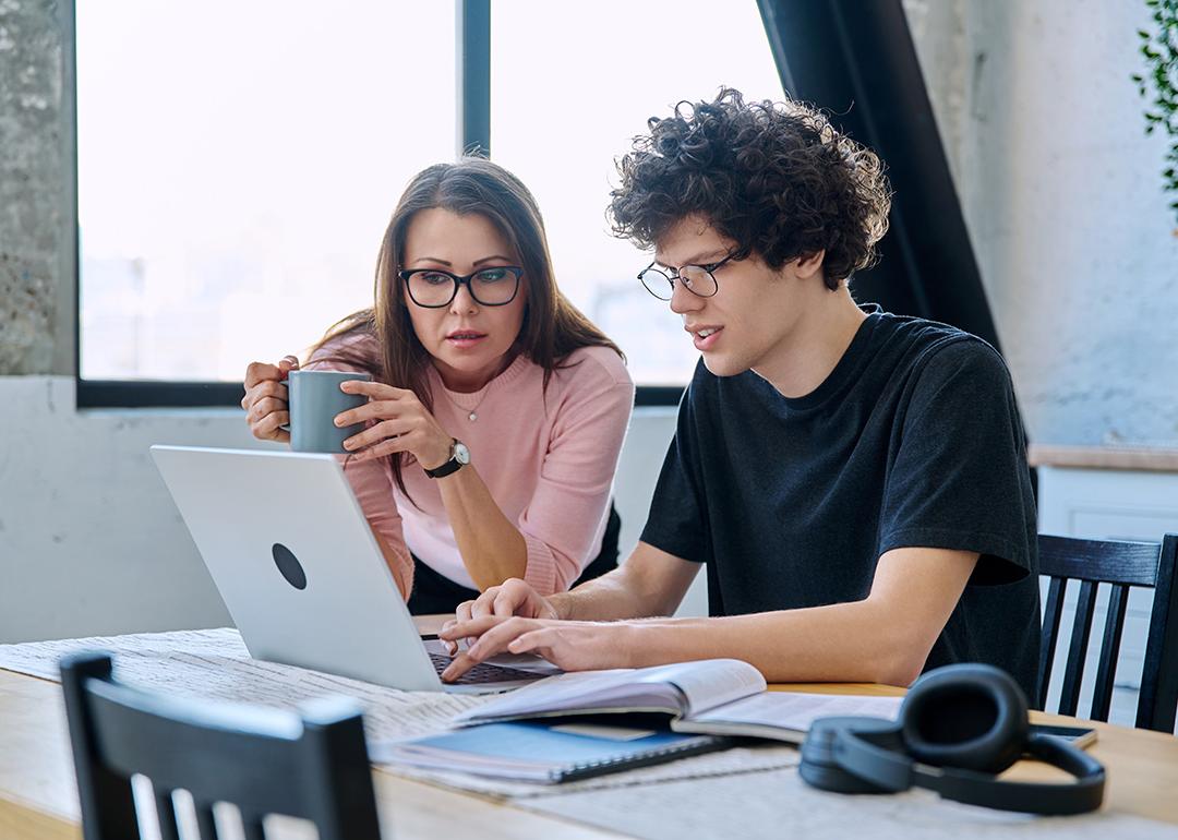A mother and her Gen Z son looking at a laptop together at home.