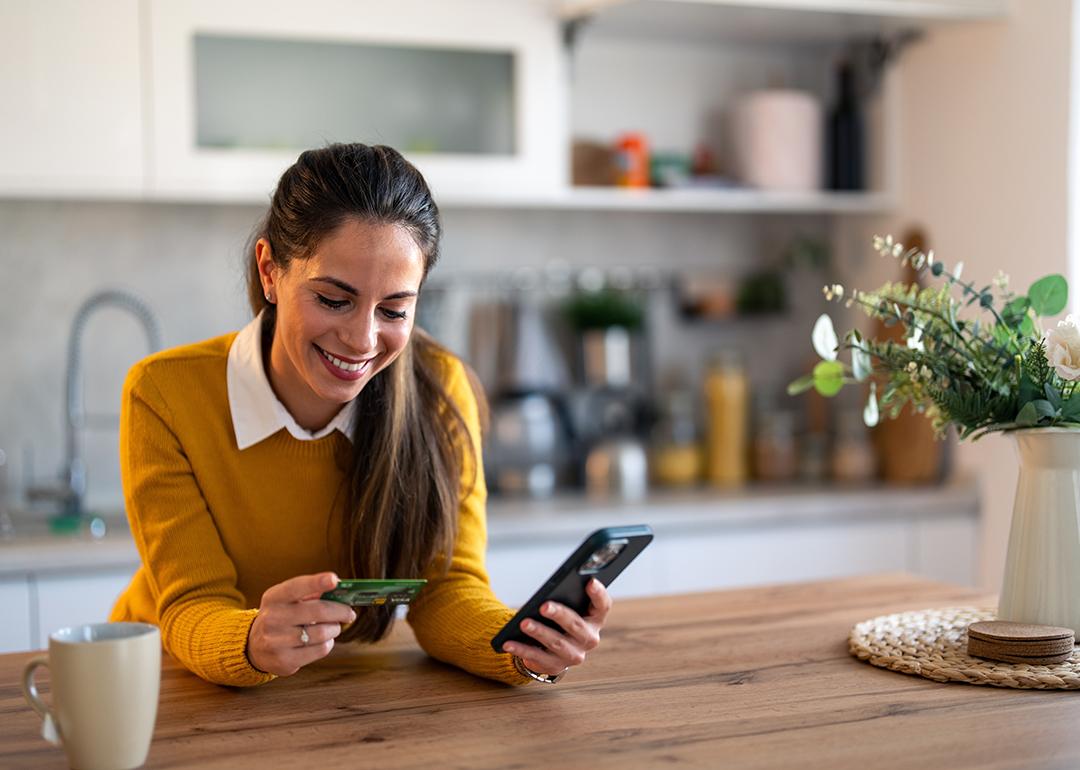A woman using a smartphone, holding a credit card, while also checking an online bank account.