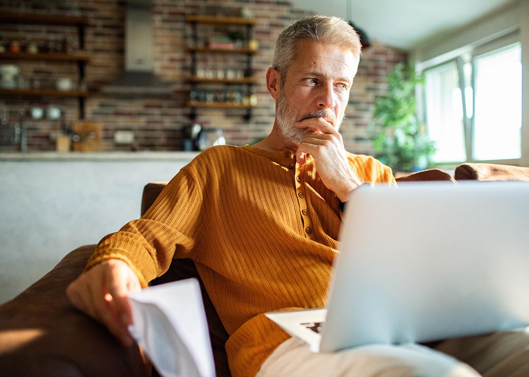 A man thinking with a laptop on his lap at home. 