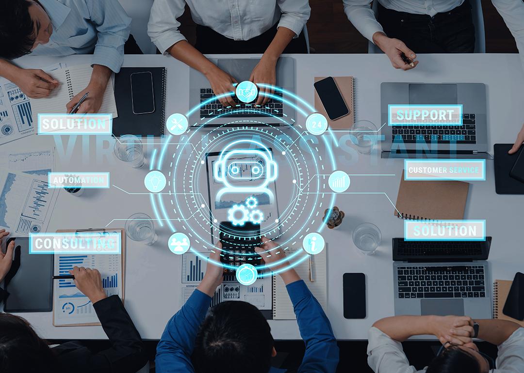 A top view of professionals engaging around a table, while using virtual assistant technology in a meeting.