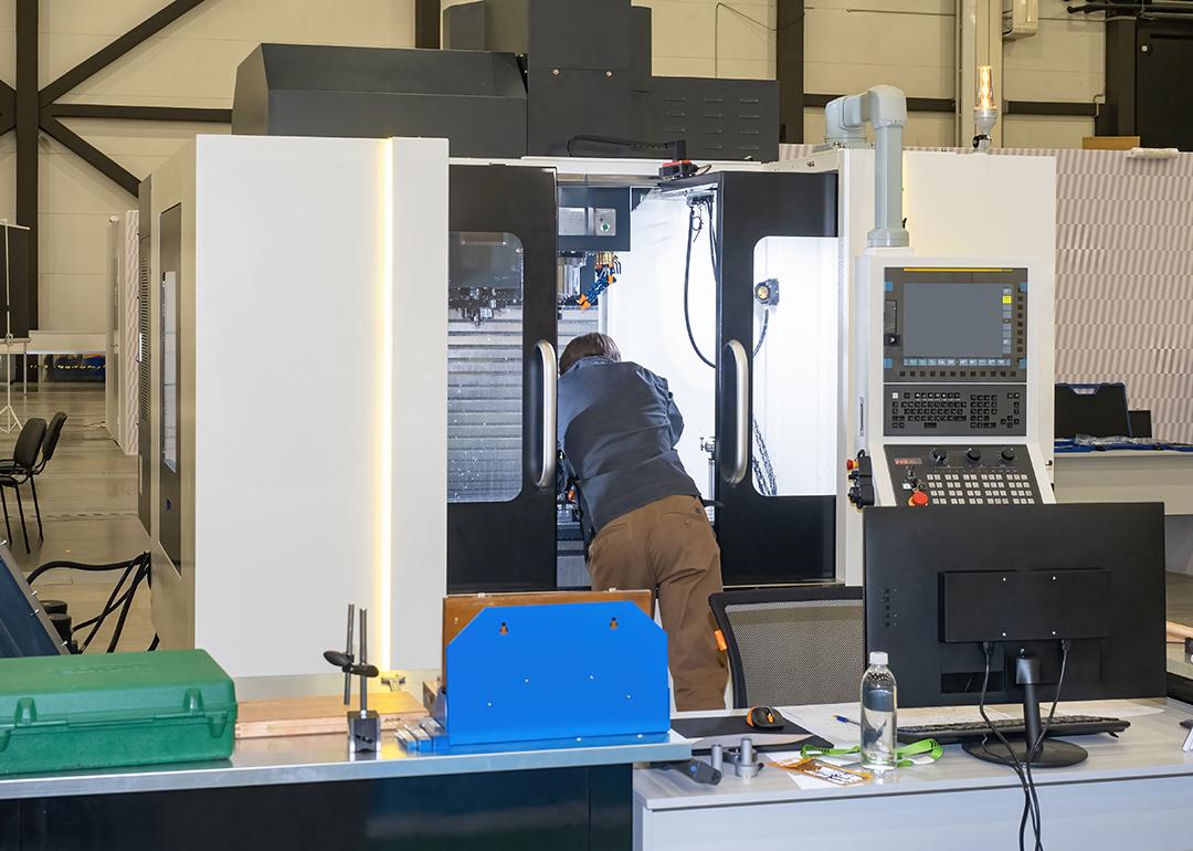 A man looking inside a CNC machine during a maintenance process in a production workshop.