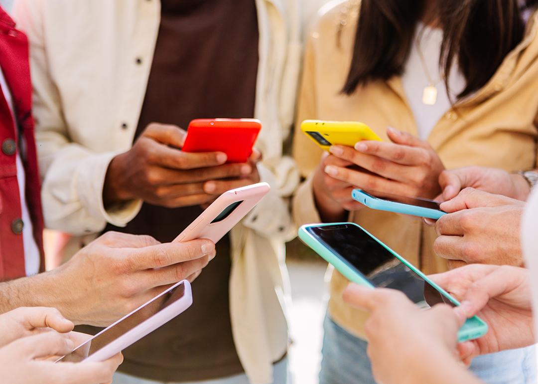 A group of young people using smartphone forming a circle outdoors.