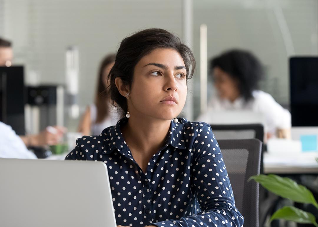 An employee looking away from a laptop in the office. 