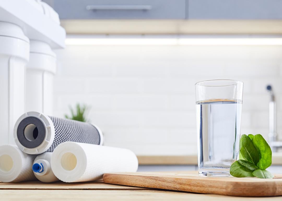 A glass of clean filtered water beside replacement filters of an osmosis water filtration system.