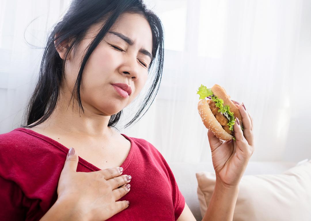 A person experiencing a heartburn while eating a burger.
