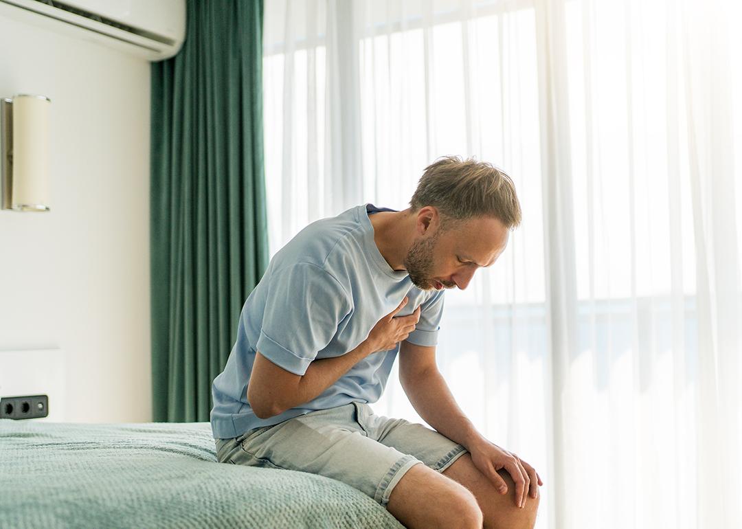 A man sitting on his bed clutching chest due to pain.