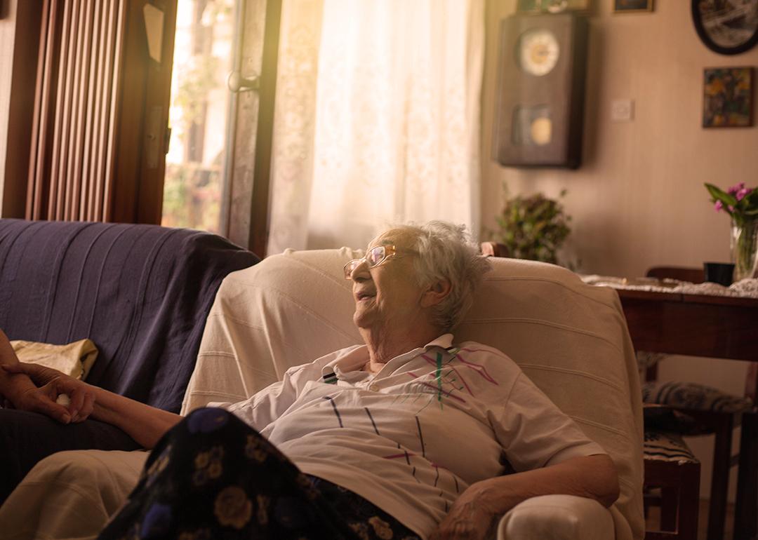 An old woman sitting on a sofa at home.