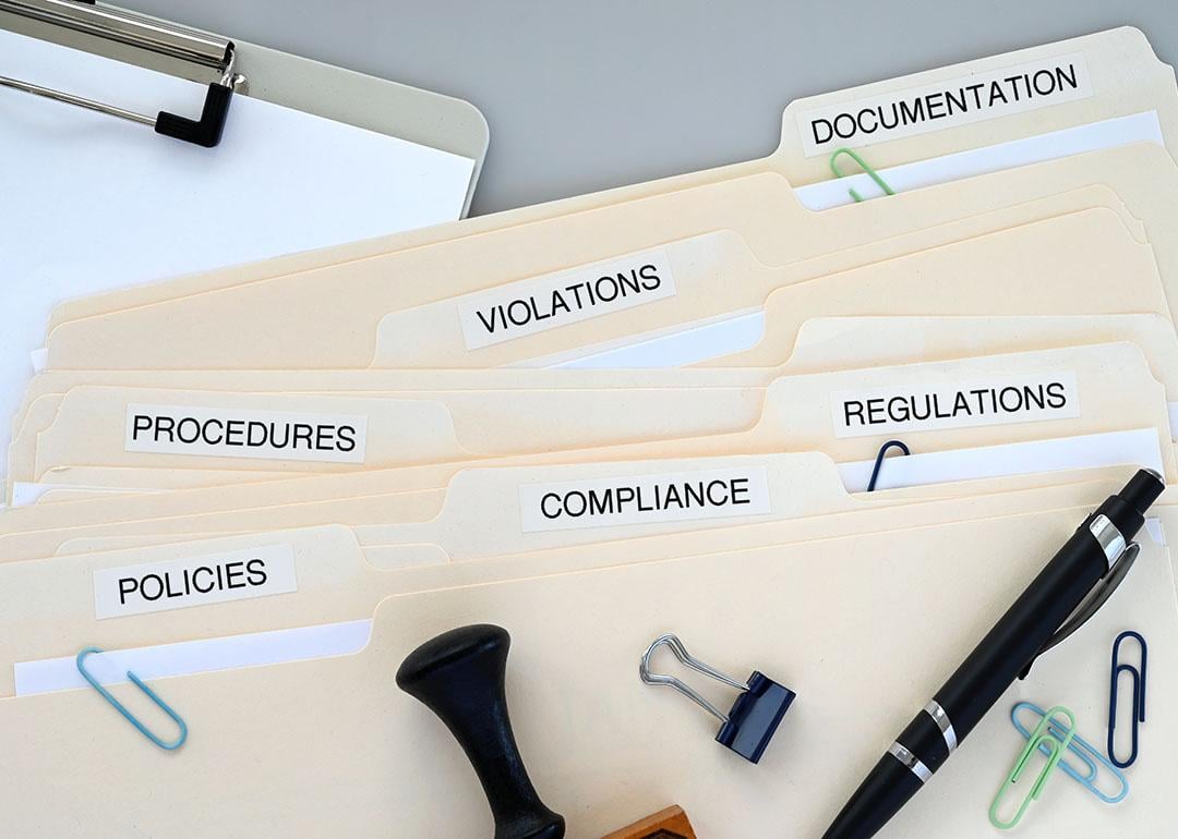 Folders of compliance and policy documents on a desk.