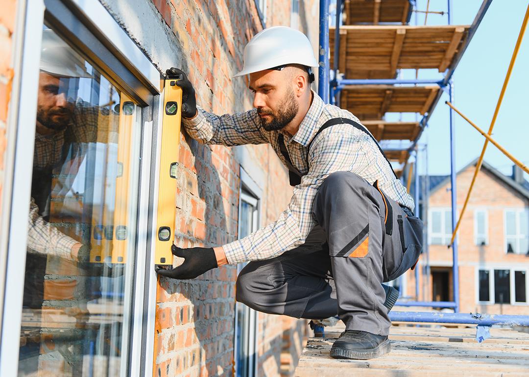 A construction worker installing a window while standing on scaffolding.