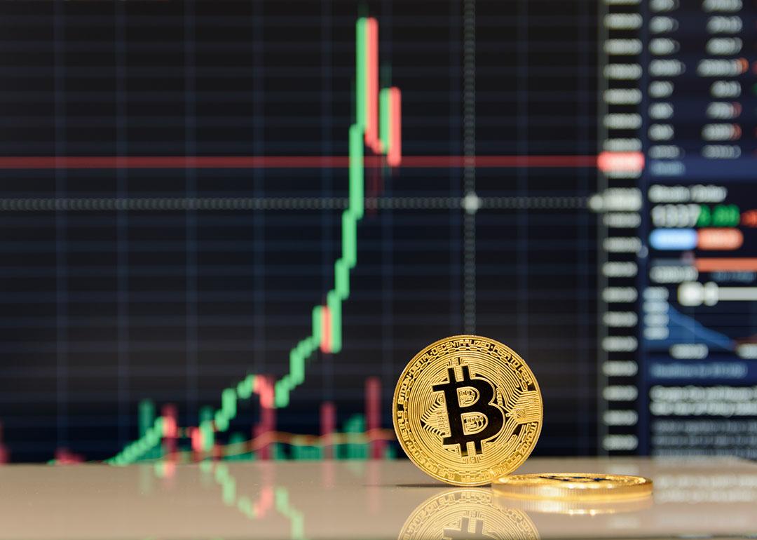 A golden bitcoin in front of stock exchange charts.