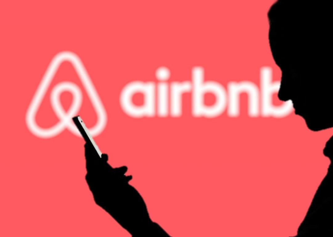 Silhouette of a man using a phone against a background showing Airbnb's logo.