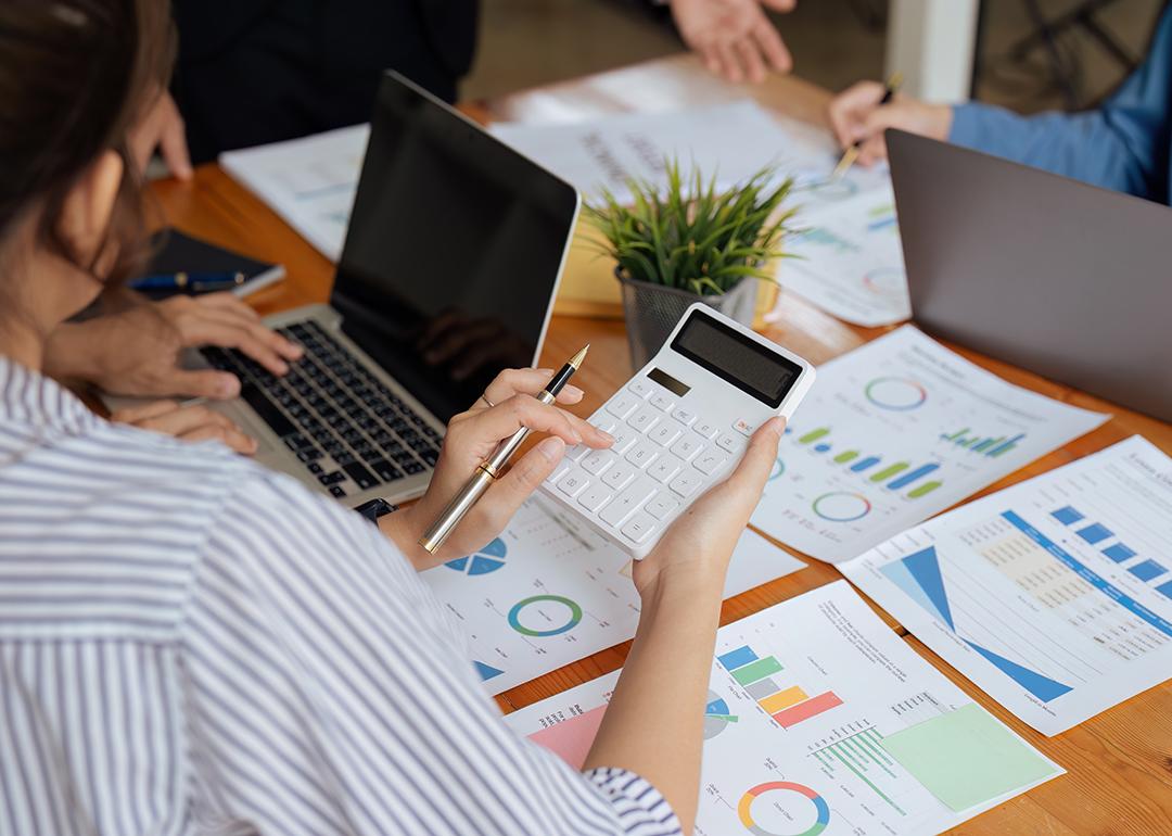 Businesswoman using a calculator while reviewing reports.