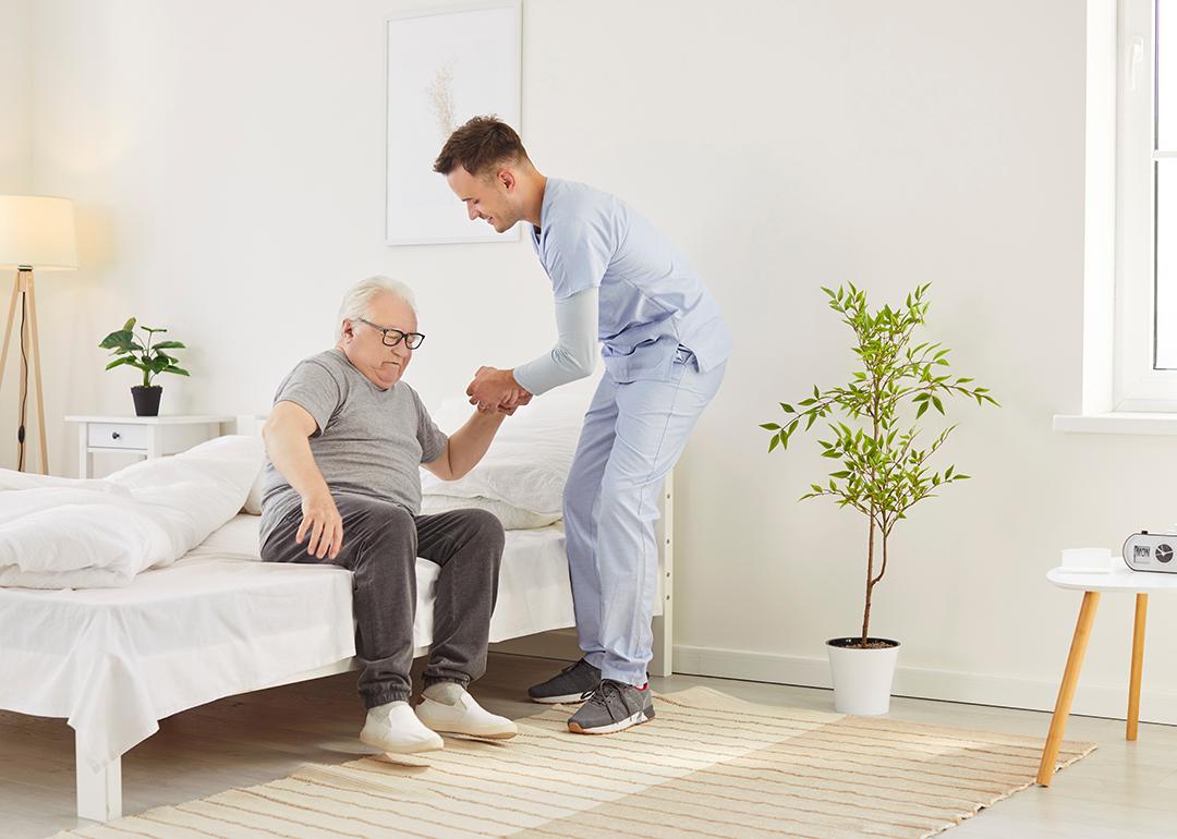 A nurse helping an elderly patient get out of bed in a nursing home. 