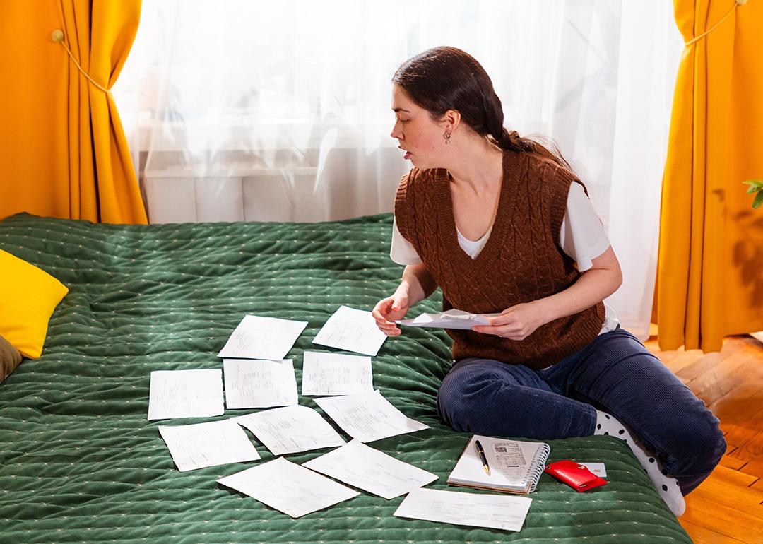 Young woman organizing bills on the bed.