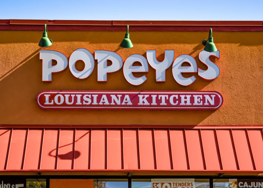 orizontal, medium closeup of "Popeyes" Louisiana Kitchen exterior facade brand and logo signage in white letters on a bright sunny day.