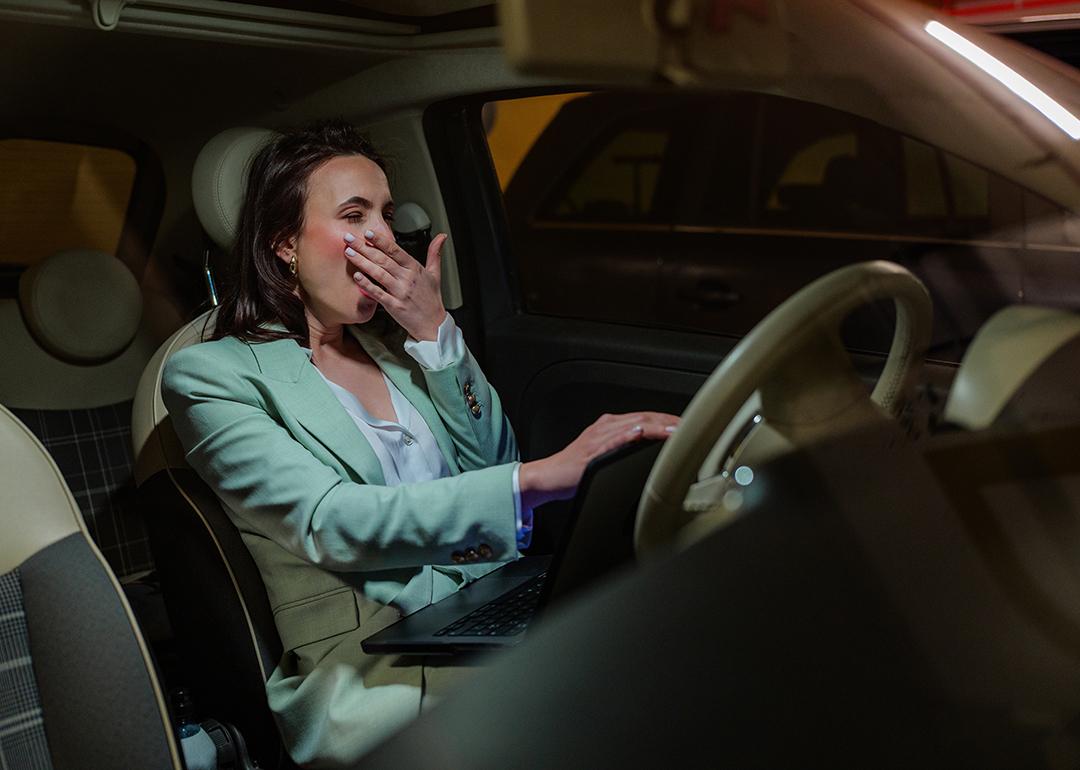 An employee yawning inside her car after work. 