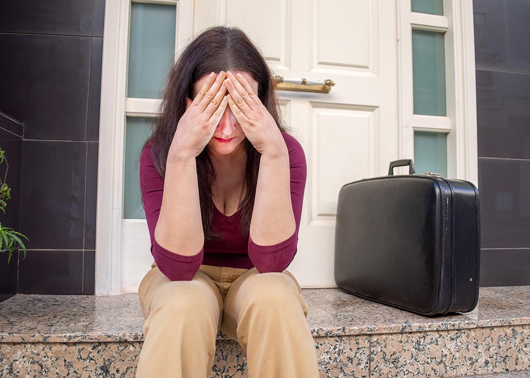 Woman sitting by the entrance of a home in a disappointed gesture.