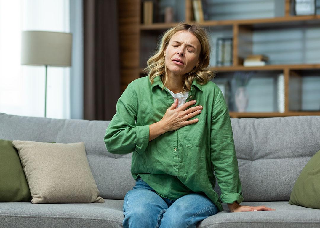 A woman sitting on a sofa holding her chest due to pain.