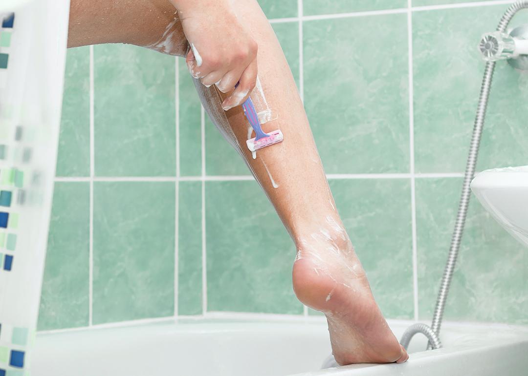 A close-up of a person shaving her leg in a bathroom. 