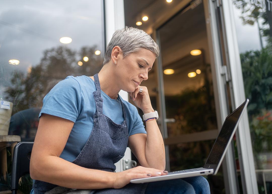 A female small business owner by the entrance of her store reviewing information on a laptop.