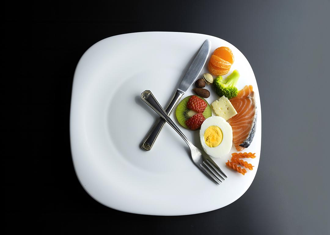 A plate of healthy ingredients simulating a clock with its hands represented by a knife and a fork as a concept of intermittent fasting.