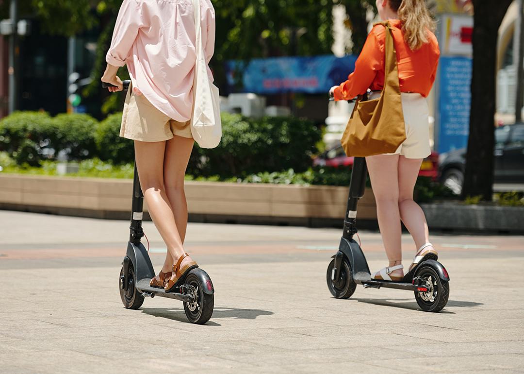 Two women riding electric scooters outdoors.
