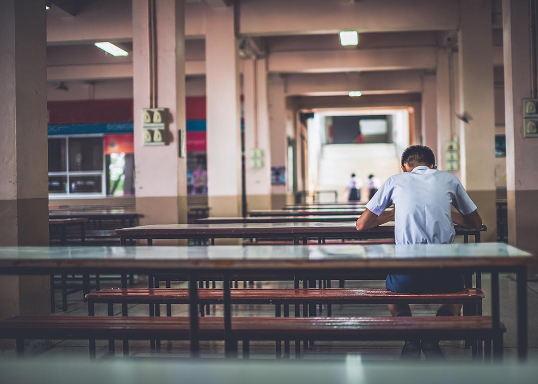 A male high school student sitting alone at a cafeteria.