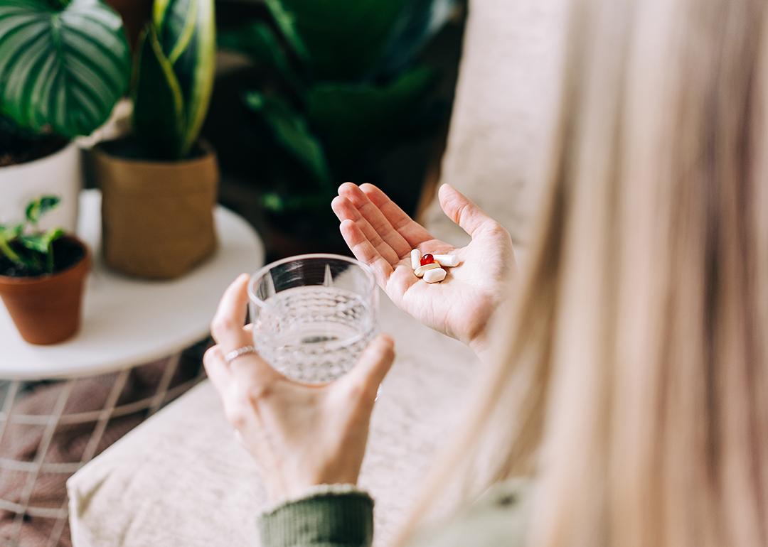 A woman holding multiple pills to drink with a glass of water.