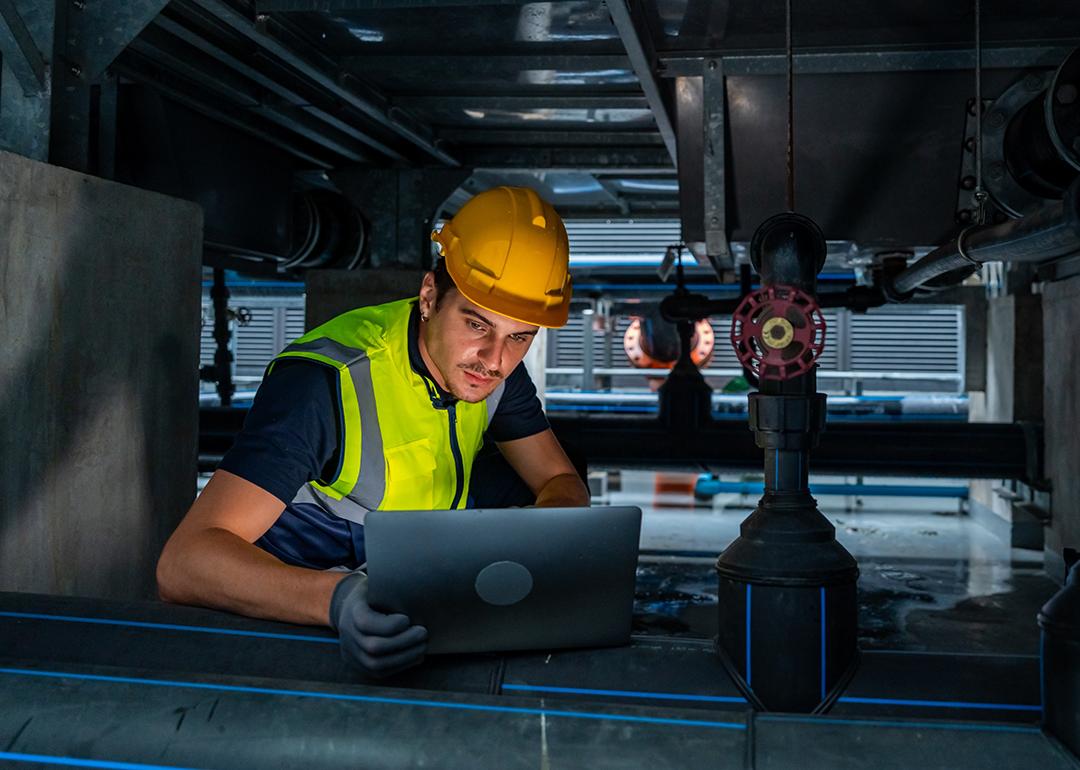 An industrial engineer viewing a laptop while checking an HVAC pipeline system.