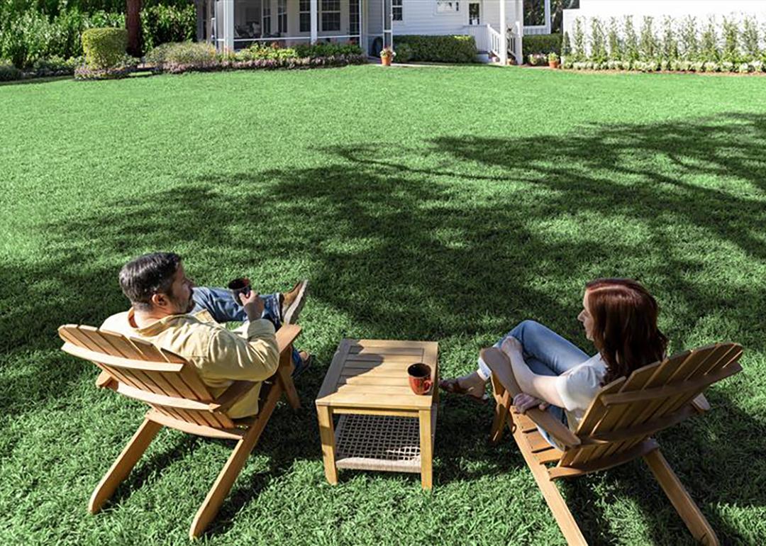 A couple sitting under the shade of trees in their backyard.