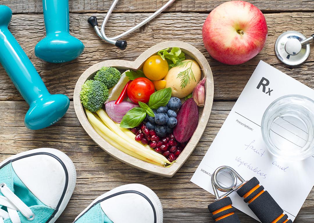 Fruits and vegetables in a heart bowl surrounded by fitness and healthy lifestyle objects.