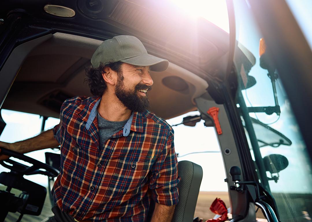 A farm worker in a tractor looking at an agricultural field.