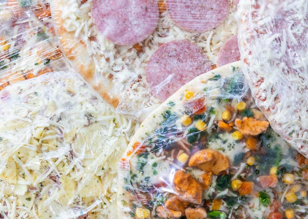 Multiple frozen pizzas wrapped in plastic stacked on each other