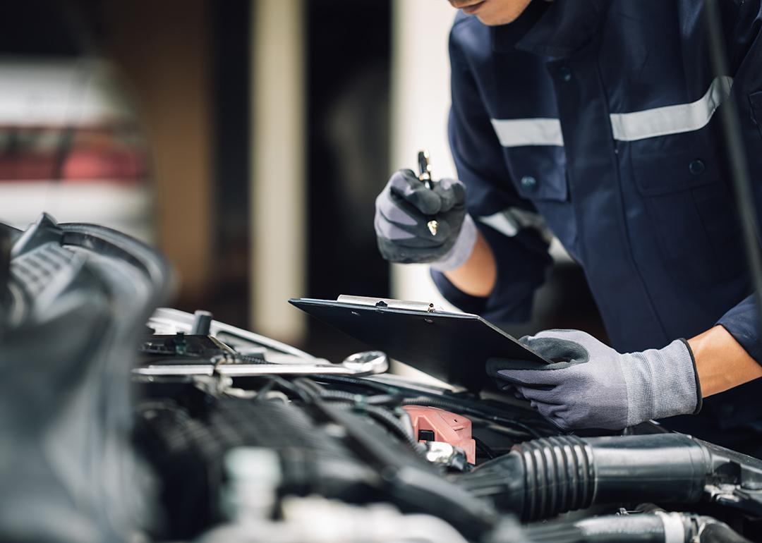 A car mechanic doing a checklist while looking at an engine.