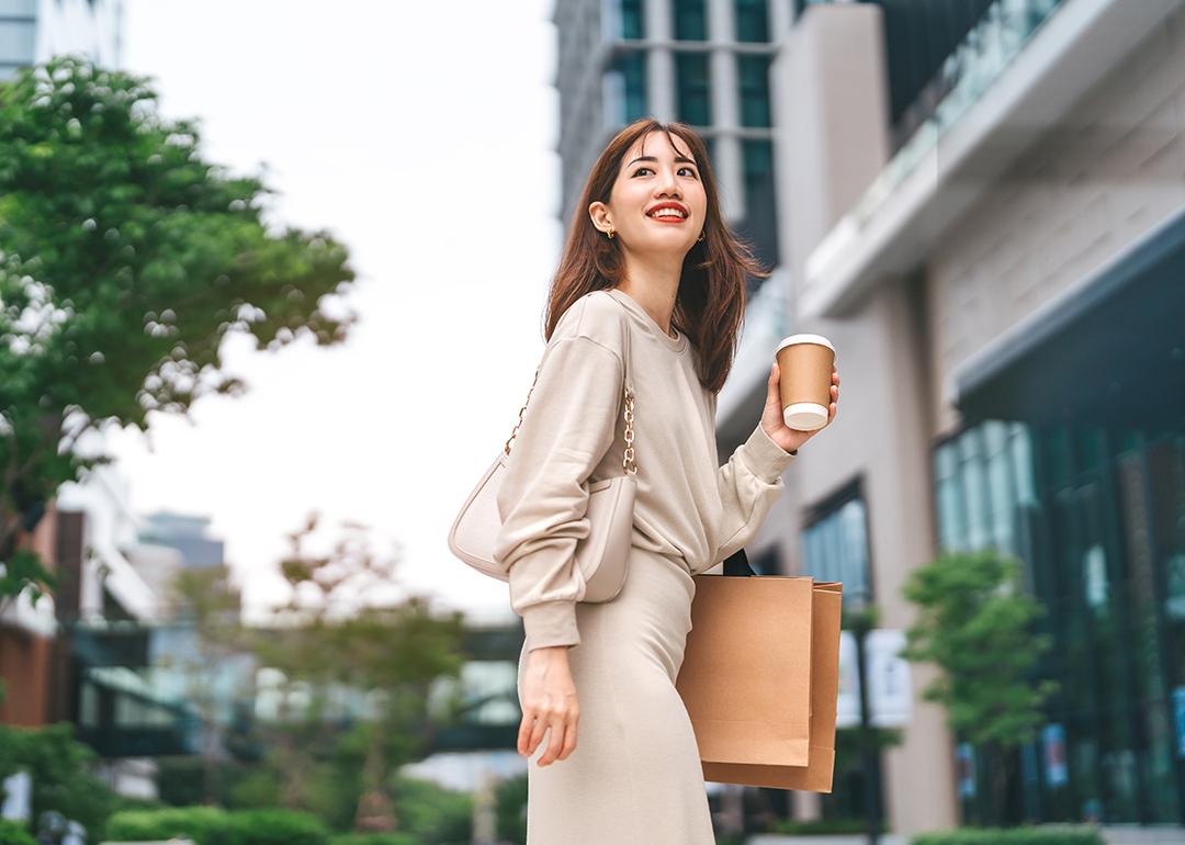 A young woman holding a cup of coffee and shopping bag outdoors.